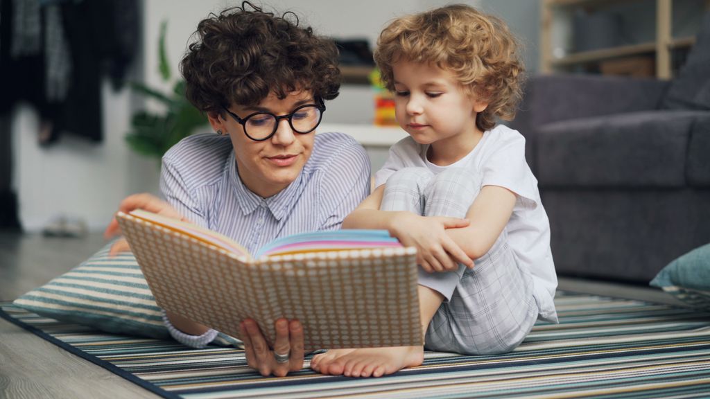 Mother and young son lying on carpet, engaged in reading a book together happily.