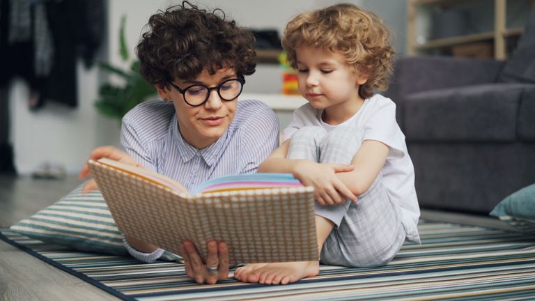 Mother and young son lying on carpet, engaged in reading a book together happily.