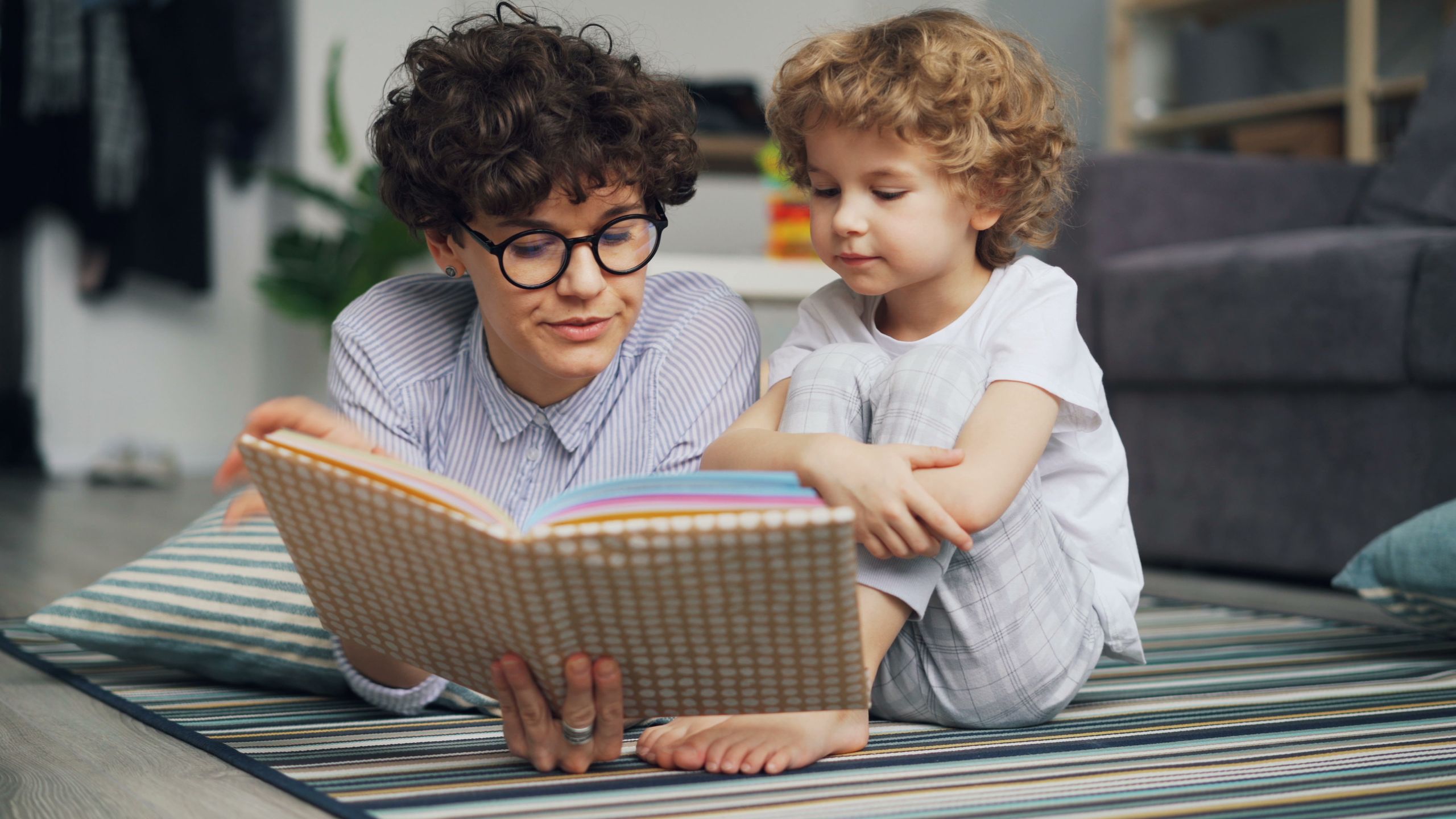 Mother and young son lying on carpet, engaged in reading a book together happily.